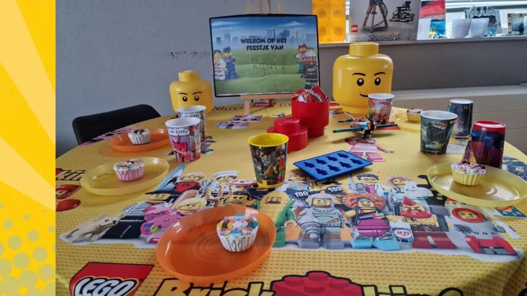 Feesttafel gedekt voor een LEGO kinderfeestje met cupcakes, bekers en LEGO hoofden als decoratie